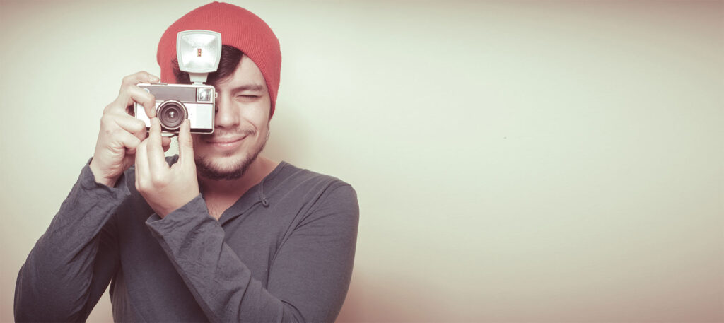 Young stylish man holding old camera on vignetting background